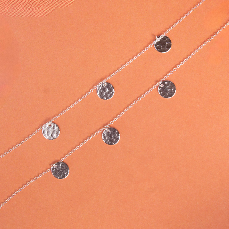 Silver bracelets with circular pendants on an orange background