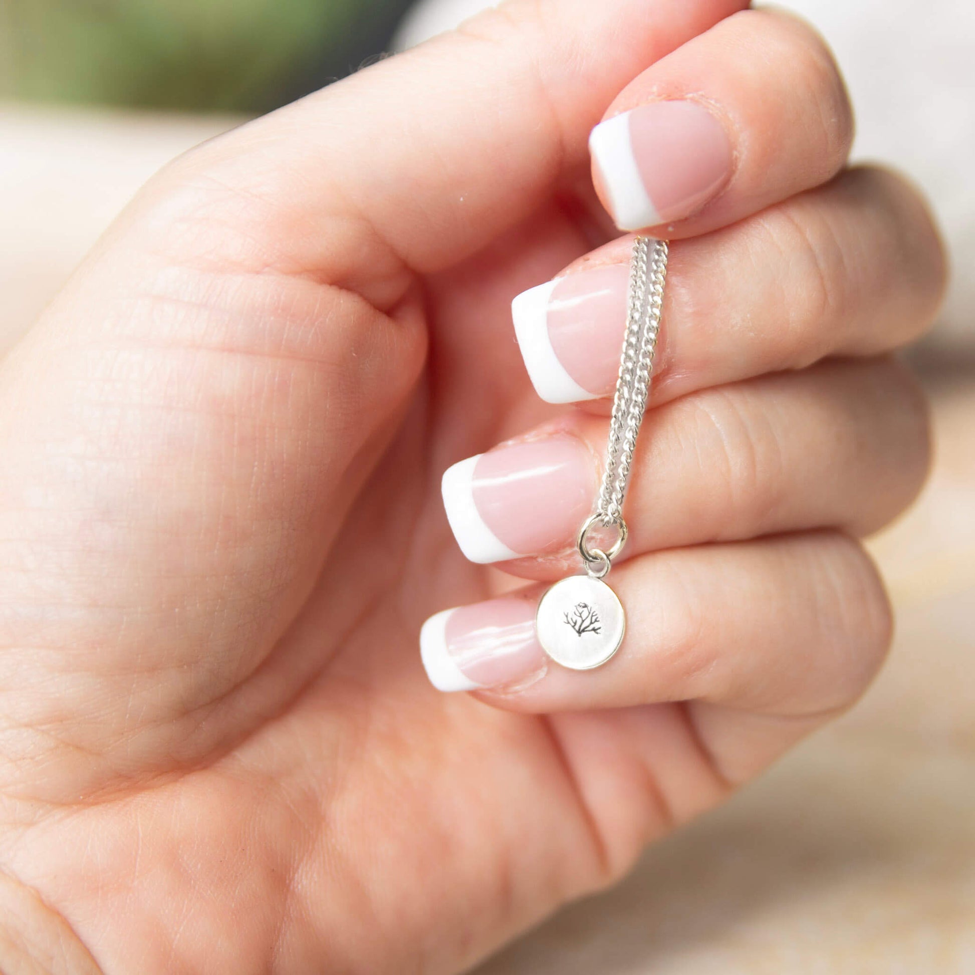 hand holding a silver necklace with a coral engraving