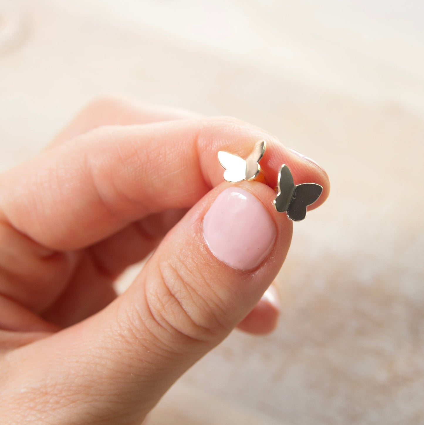 hand holding silver butterfly stud earrings