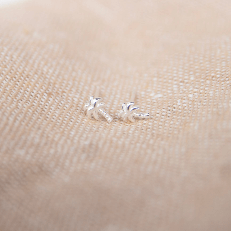 Silver palm tree earrings on a beige fabric background