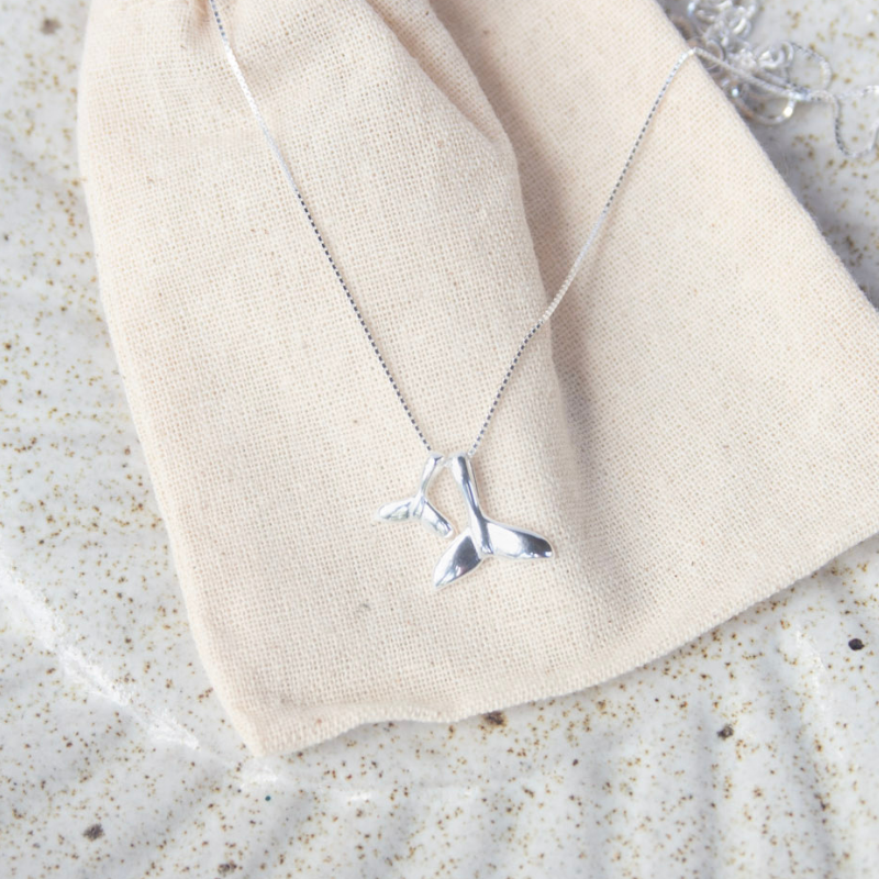 Silver whale tail necklace on a beige fabric background