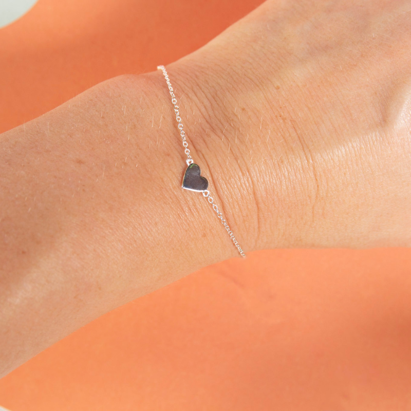 Silver bracelet with a heart charm on a wrist against an orange background