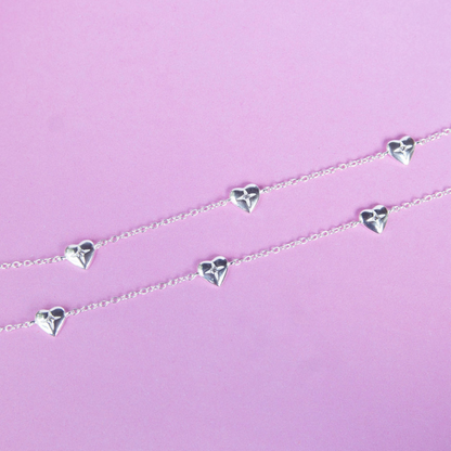 Silver heart-shaped necklace on a pink background