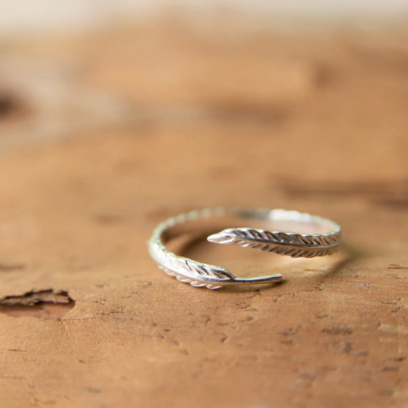 Silver open ring with feather design on a brown surface