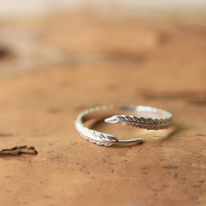 Silver open ring with feather design on a brown surface