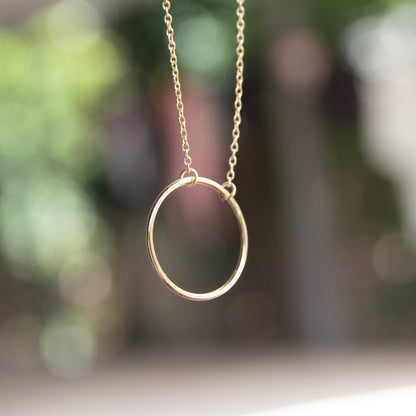 Gold necklace with a circular pendant against a blurred natural background
