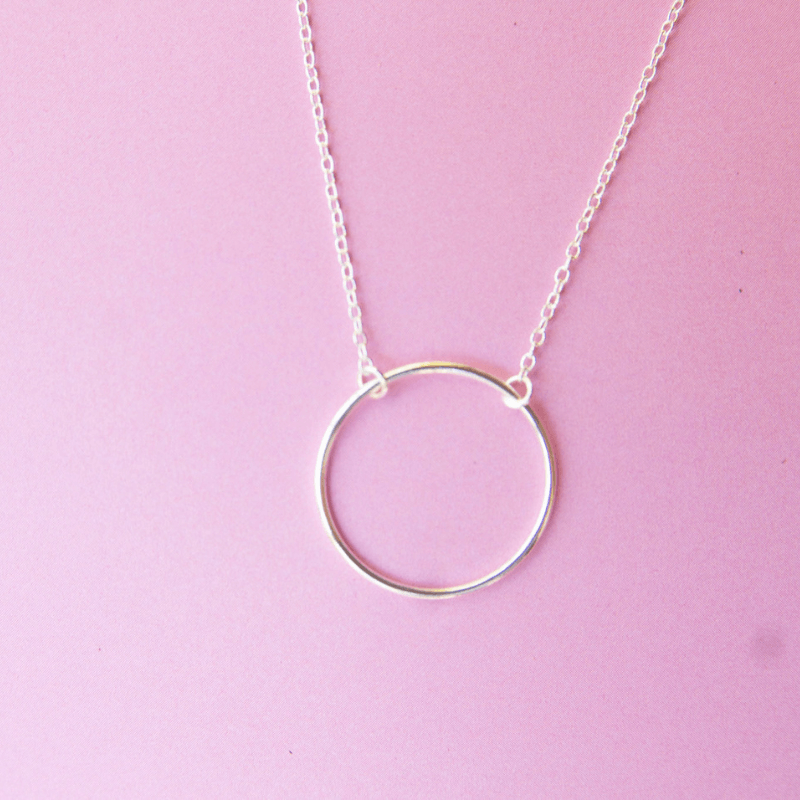 Silver circle pendant necklace on a pink background