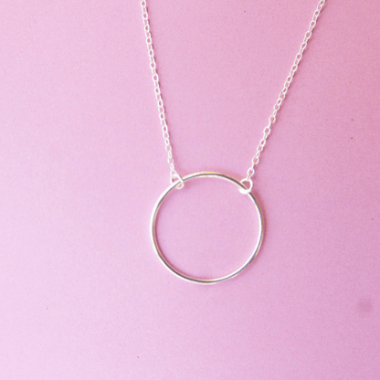 Silver circle pendant necklace on a pink background