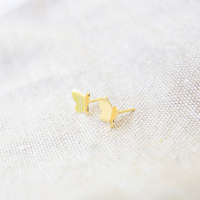 Gold butterfly earrings on a textured white surface