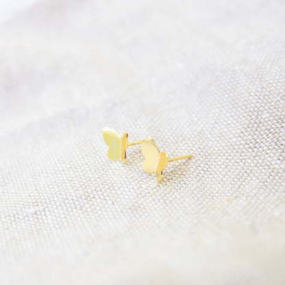 Gold butterfly earrings on a textured white surface