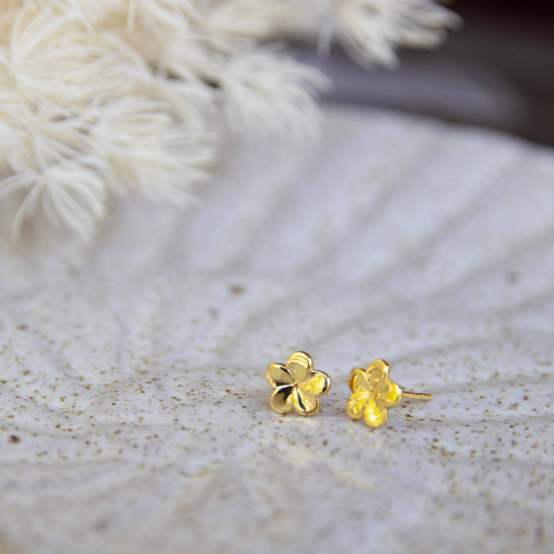 Gold flower-shaped earrings on a textured surface with blurred white flowers in the background