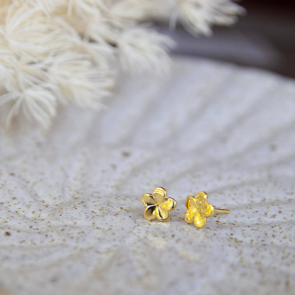 Gold flower-shaped earrings on a textured surface with blurred white flowers in the background