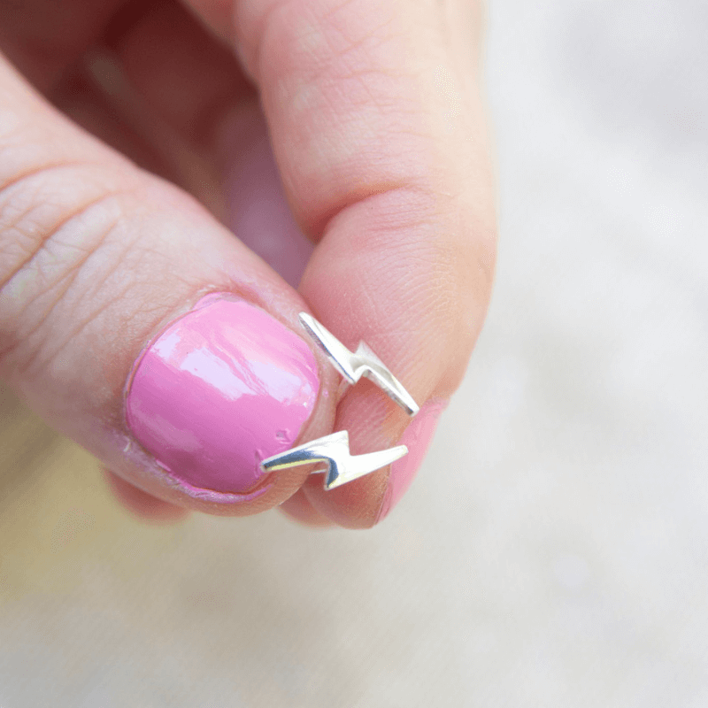 Silver earring being held between fingers with pink nail polish on a light background