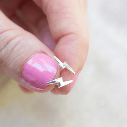 Silver earring being held between fingers with pink nail polish on a light background
