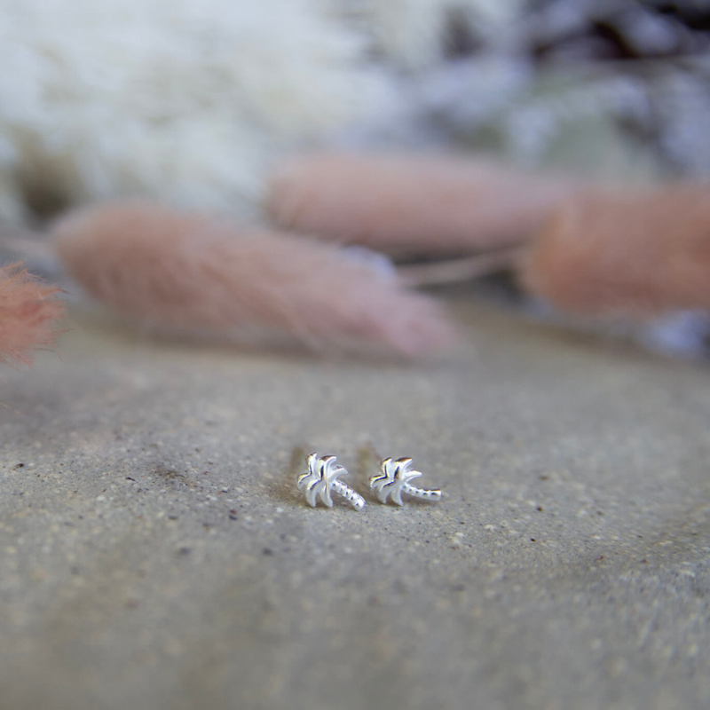 Silver palm-shaped earrings on a textured surface with a blurred background