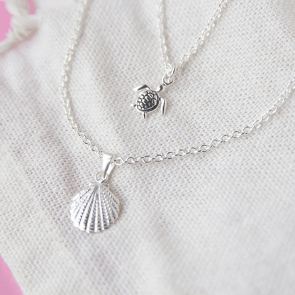 Silver necklace with shell and turtle pendant on a white background