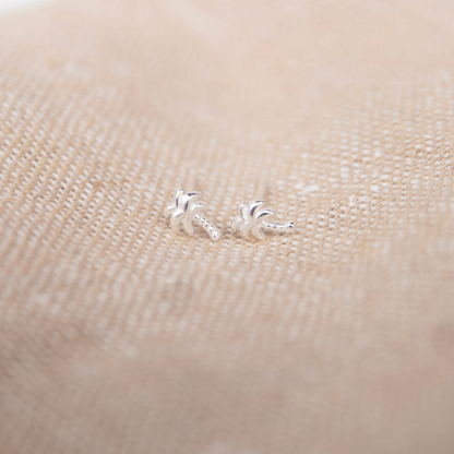 Silver palm tree earrings on a beige fabric background