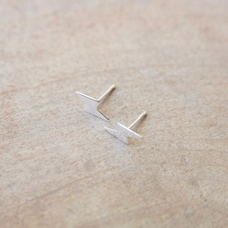 Silver lightning-shaped earrings on a beige surface