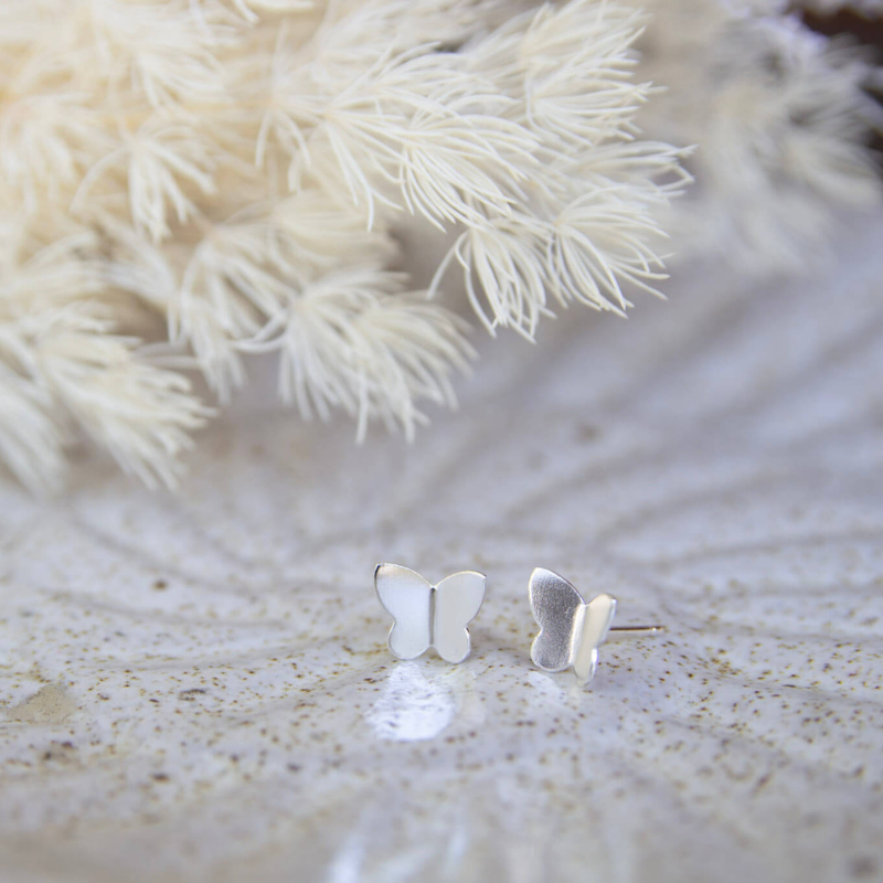 Silver butterfly earrings on a textured surface with a soft white background