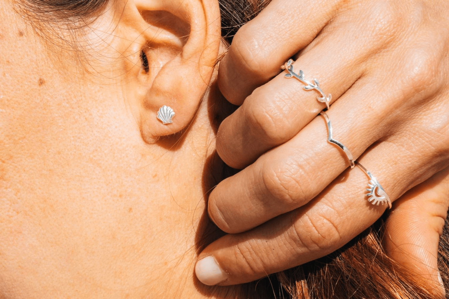 Close-up of a person wearing silver earrings and rings on a blurred background